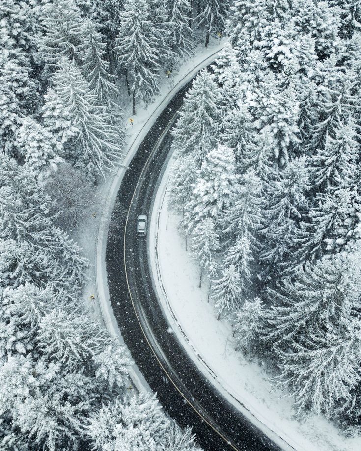 Winter Driving Tips _ SimpleTire Aerial view of a snowy road winding through a forest in winter, with snow-covered trees and a lone car driving. | Sky Rye Design Aerial view of a snowy road winding through a forest in winter, with snow-covered trees and a lone car driving.