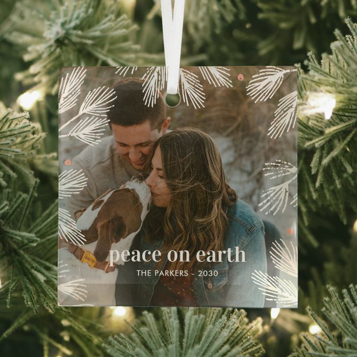 Winter Pines Custom Photo Christmas Ornament Family Christmas ornament with peace on earth message hanging on a tree branch, featuring a couple and their dog. | Sky Rye Design Family Christmas ornament with peace on earth message hanging on a tree branch, featuring a couple and their dog.