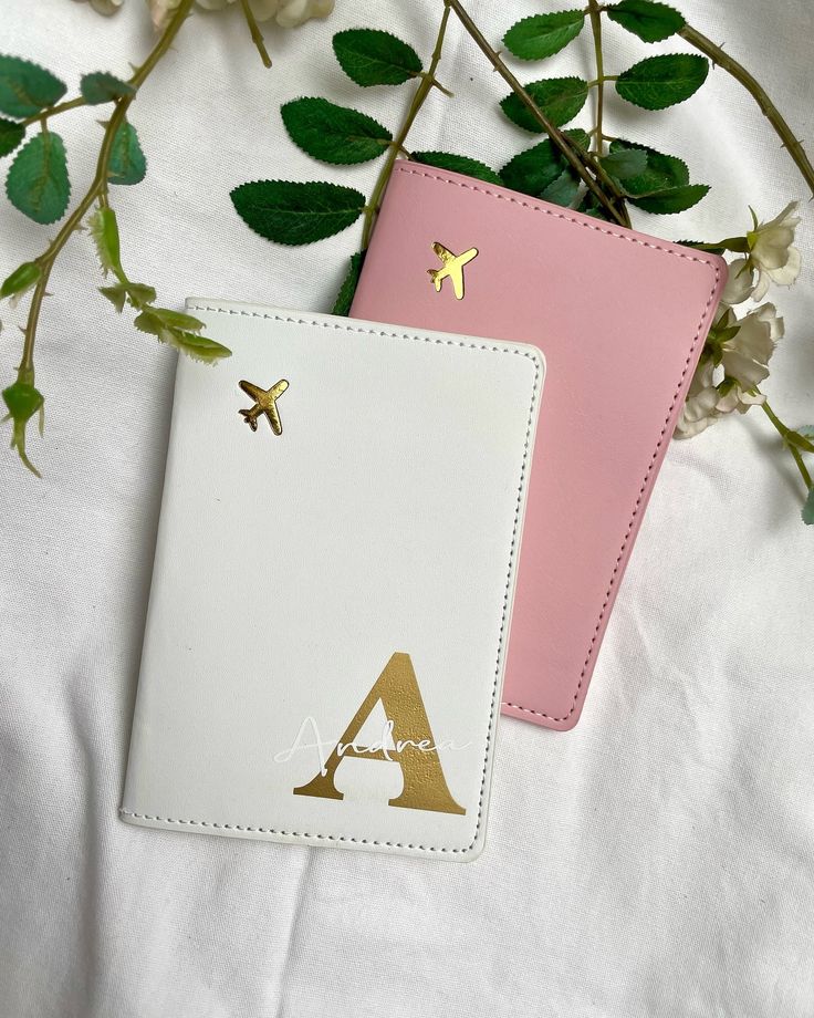 Two stylish passport holders, one white and one pink, adorned with airplane symbols and leafy accents.