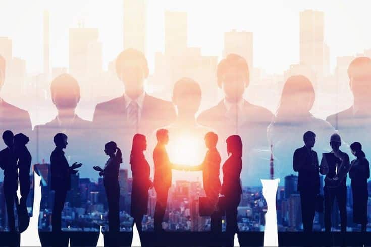 Business professionals interacting and shaking hands with a city skyline background, symbolizing partnership and teamwork.