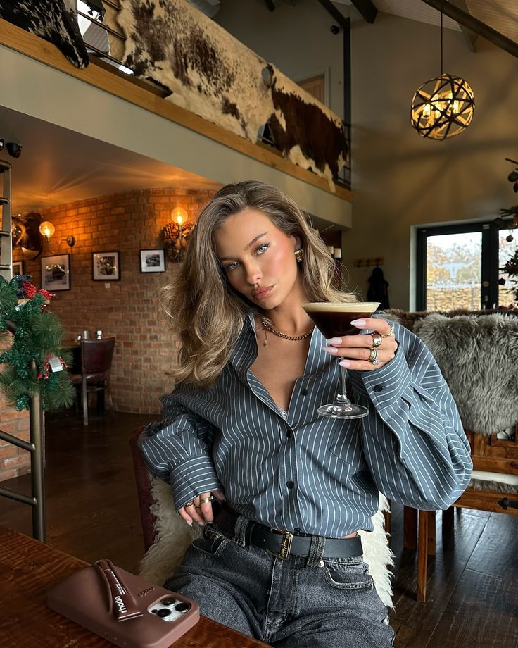 Woman in striped shirt enjoying a cocktail in a stylish, cozy cafe with rustic decor.