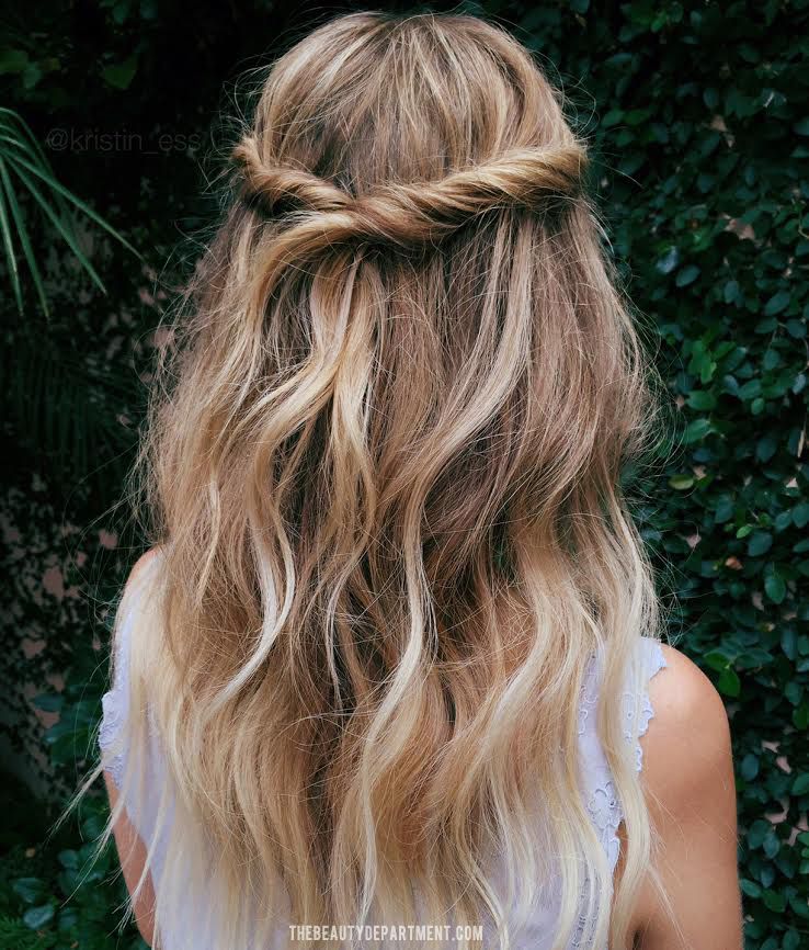 Woman with wavy, blonde half-up hairstyle against a leafy background. Stylish and elegant hair inspiration.