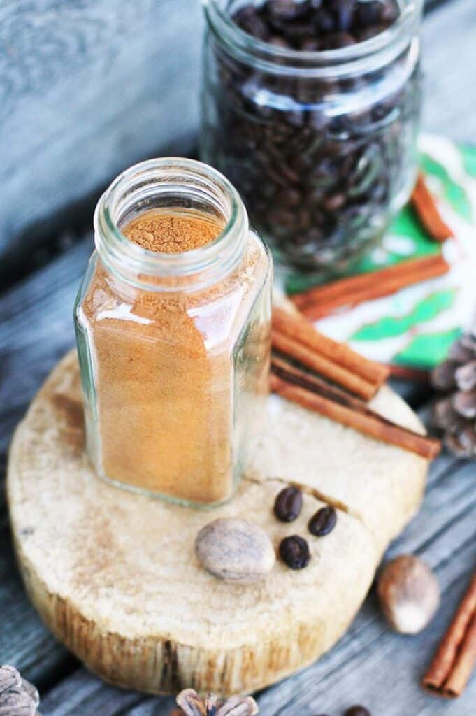 a4b9b5ef-7932-49a1-af61-95f90dc67584 Glass jar of cinnamon on a wooden board with coffee beans, nutmeg, and cinnamon sticks. Rustic kitchen spices. | Sky Rye Design Glass jar of cinnamon on a wooden board with coffee beans, nutmeg, and cinnamon sticks. Rustic kitchen spices.