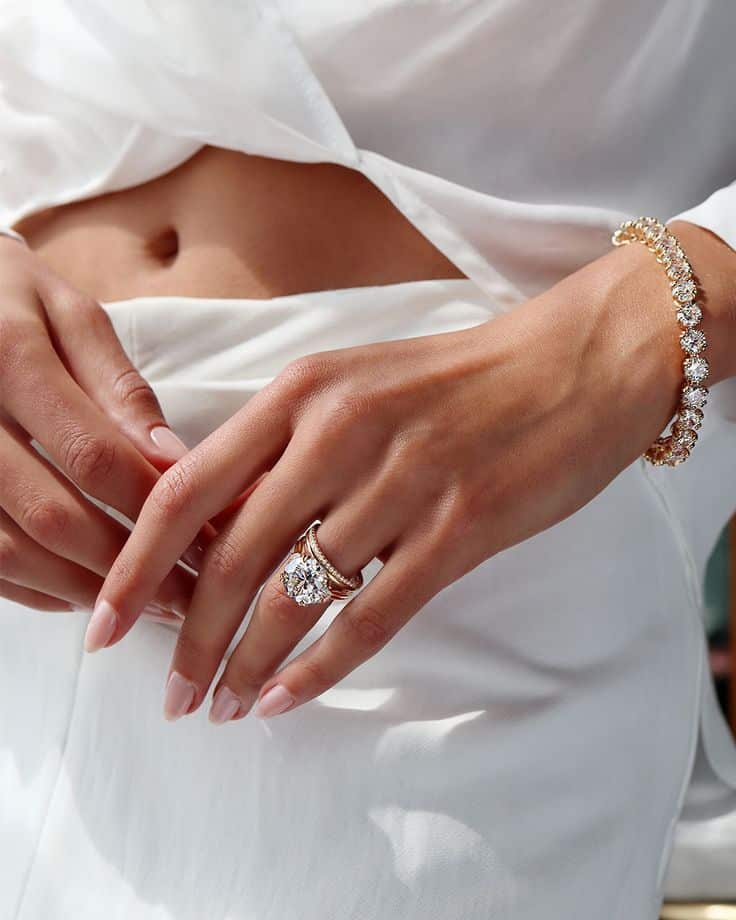 a4d8b52e-e3a1-40cc-8609-b51107e3ffc3 Woman's hand with an elegant diamond ring and bracelet against a white outfit. | Sky Rye Design Woman's hand with an elegant diamond ring and bracelet against a white outfit.