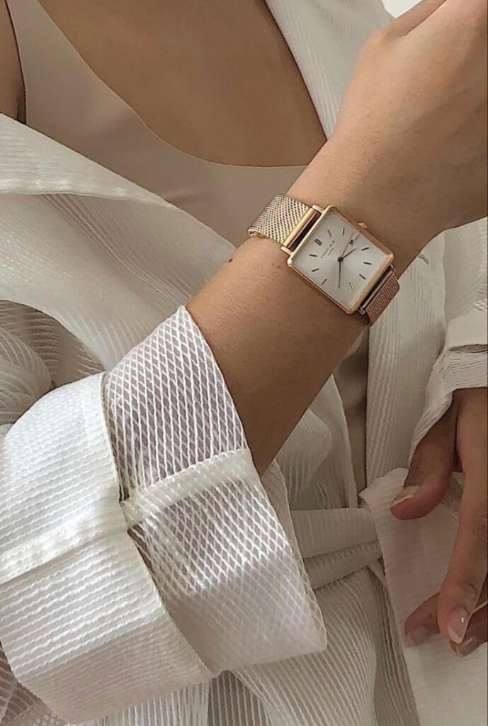 a756ff60-767e-4573-b846-49ac4c194abc Elegant gold mesh wristwatch on a person's arm, featuring a minimalist white dial, paired with a chic textured outfit. | Sky Rye Design Elegant gold mesh wristwatch on a person's arm, featuring a minimalist white dial, paired with a chic textured outfit.