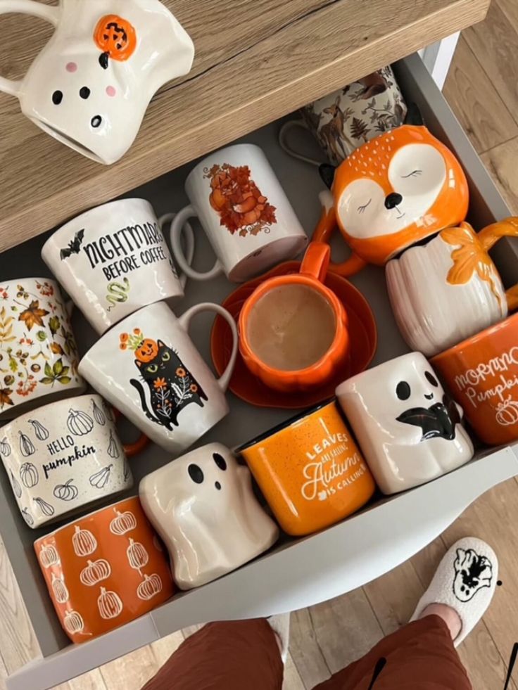 Drawer with assorted Halloween and autumn-themed mugs, including pumpkins, ghosts, and a fox design. Cozy seasonal vibes.