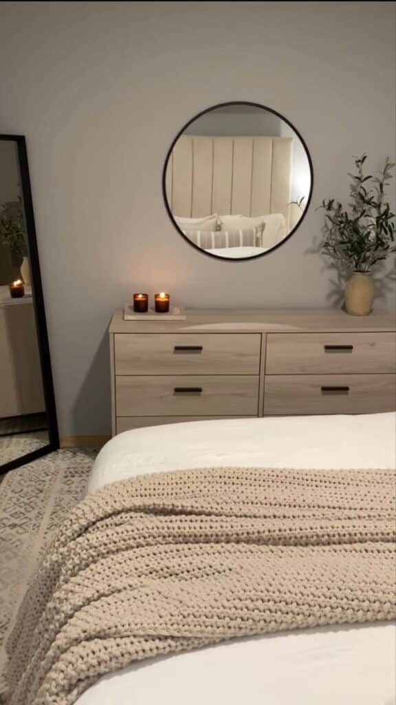ade1607c-518a-45f9-9c3f-e2ace2cf3899 Cozy bedroom with round mirror, wooden dresser, candles, and knit blanket for a warm, inviting ambiance. | Sky Rye Design Cozy bedroom with round mirror, wooden dresser, candles, and knit blanket for a warm, inviting ambiance.