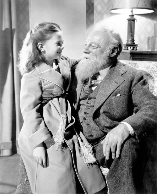Little girl smiling at elderly man in a suit, sitting together in a cozy room.