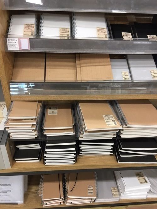 Spiral-bound notebooks on shelves, featuring various tan and black covers in a stationery store display.