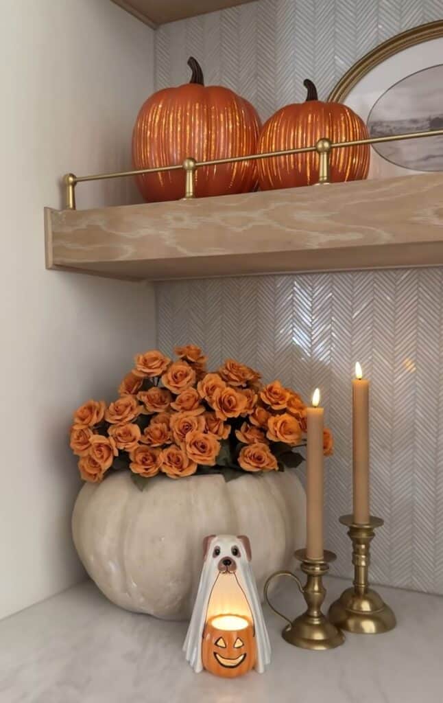 Elegant autumn decor with orange pumpkins, flowers, candle, and dog-themed holder on a marble countertop.