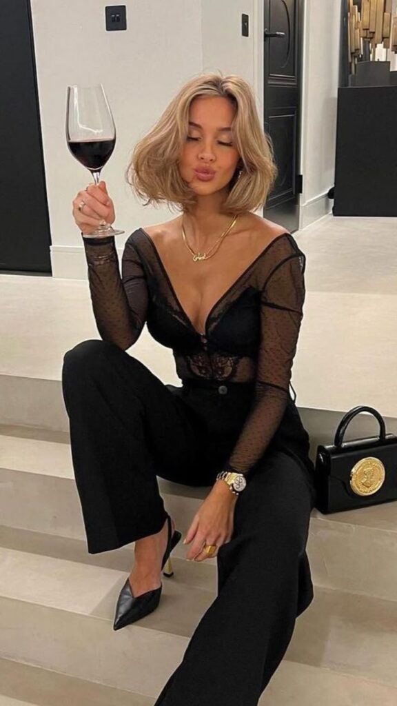 Stylish woman in black outfit sitting with a glass of red wine, chic fashion and elegance in modern setting.