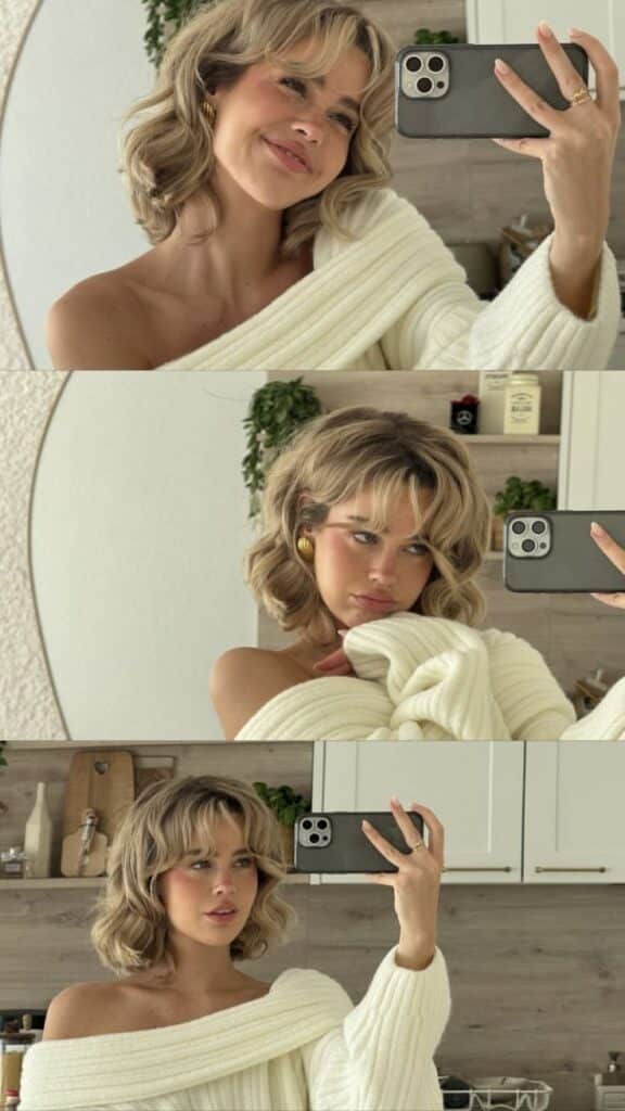Woman in cozy sweater taking mirror selfies in stylish kitchen setup.