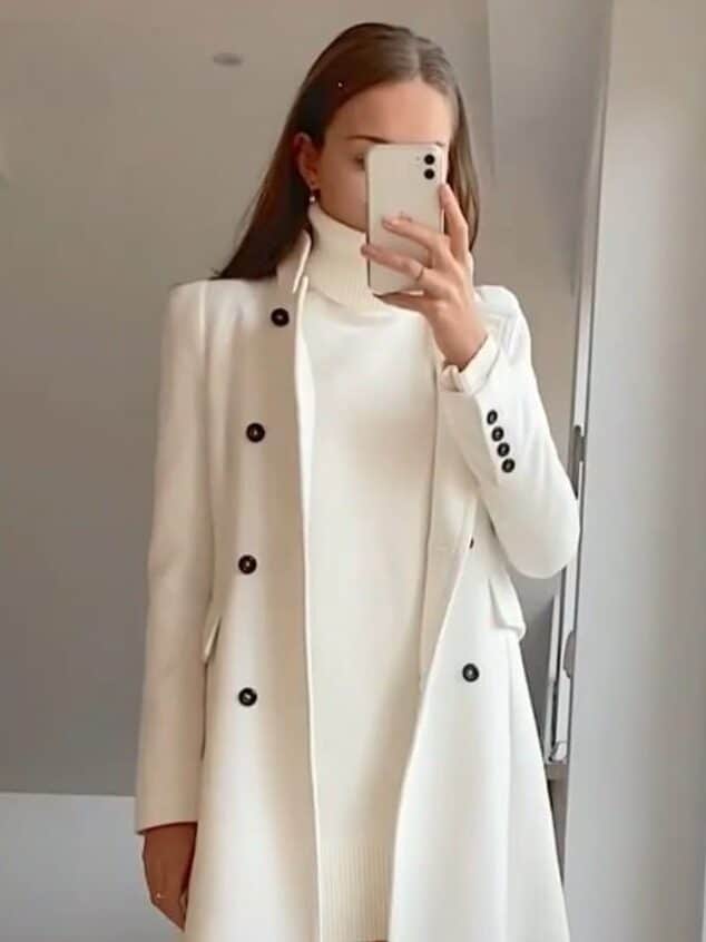 b5ca973e-a28c-4f85-84d7-9672117f615e Woman in stylish white coat and turtleneck dress, taking a mirror selfie. Brown knee-high boots complete the look. | Sky Rye Design Woman in stylish white coat and turtleneck dress, taking a mirror selfie. Brown knee-high boots complete the look.