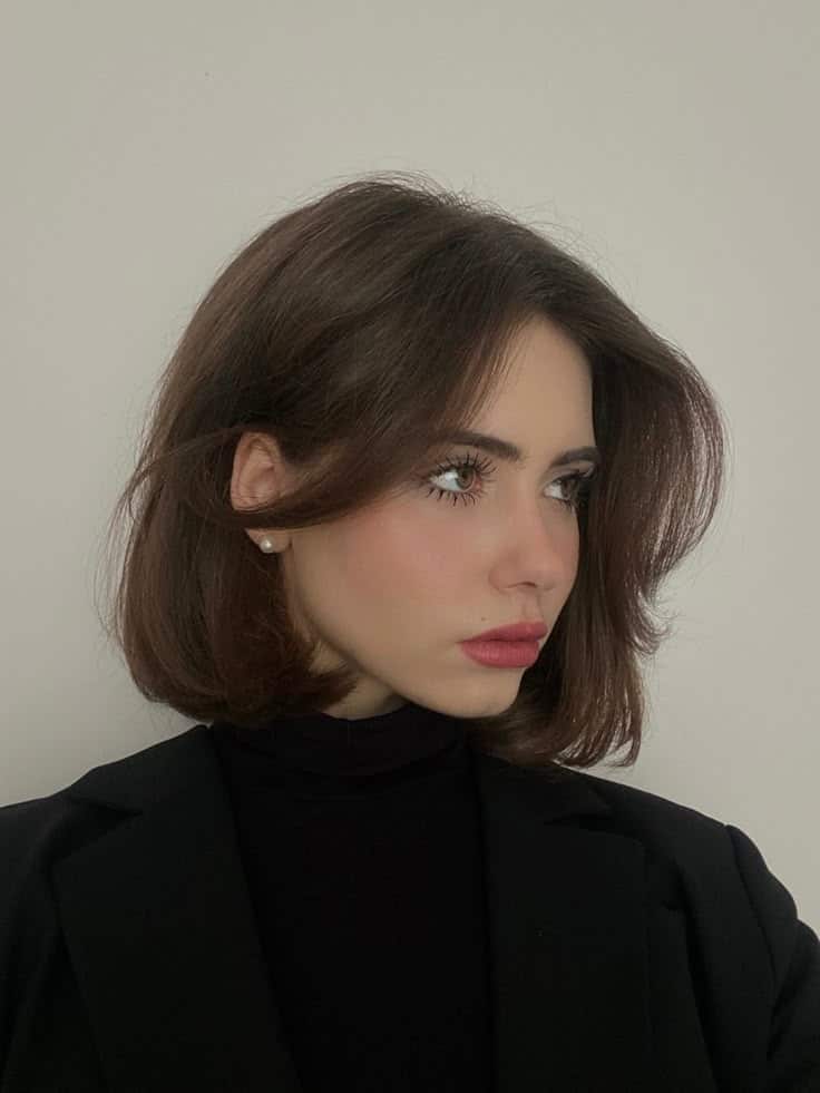 Young woman with shoulder-length dark hair wearing a black blazer, looking to the side against a neutral background.