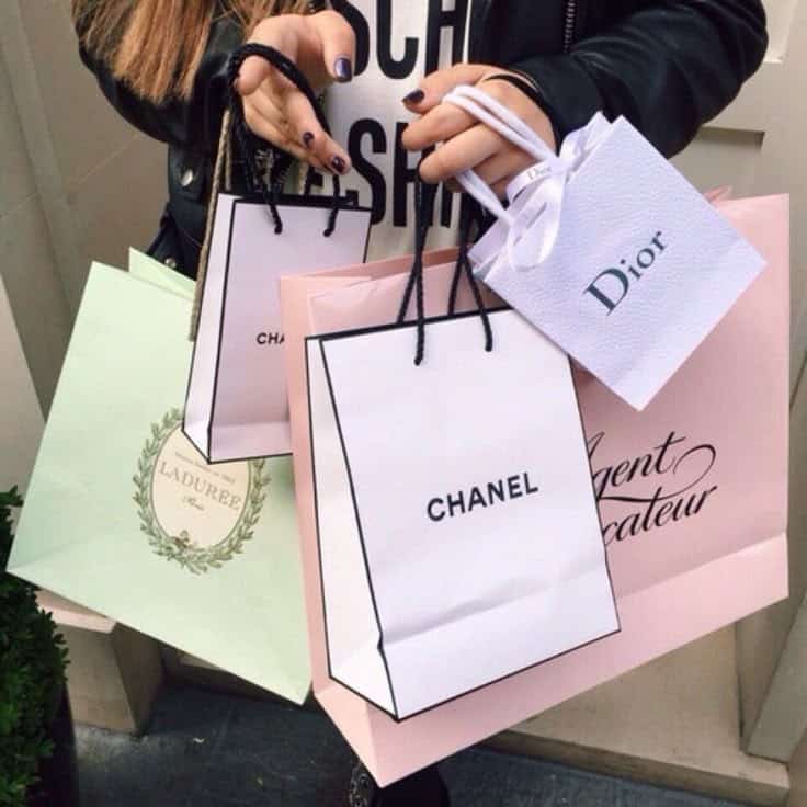 Person holding luxury shopping bags from Chanel, Dior, Ladurée, and Agent Provocateur.
