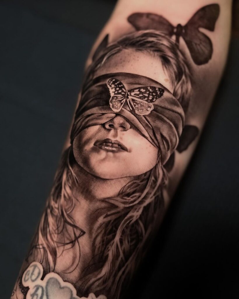 Tattoo of a blindfolded woman with butterflies on her face and around, symbolizing transformation and mystery.