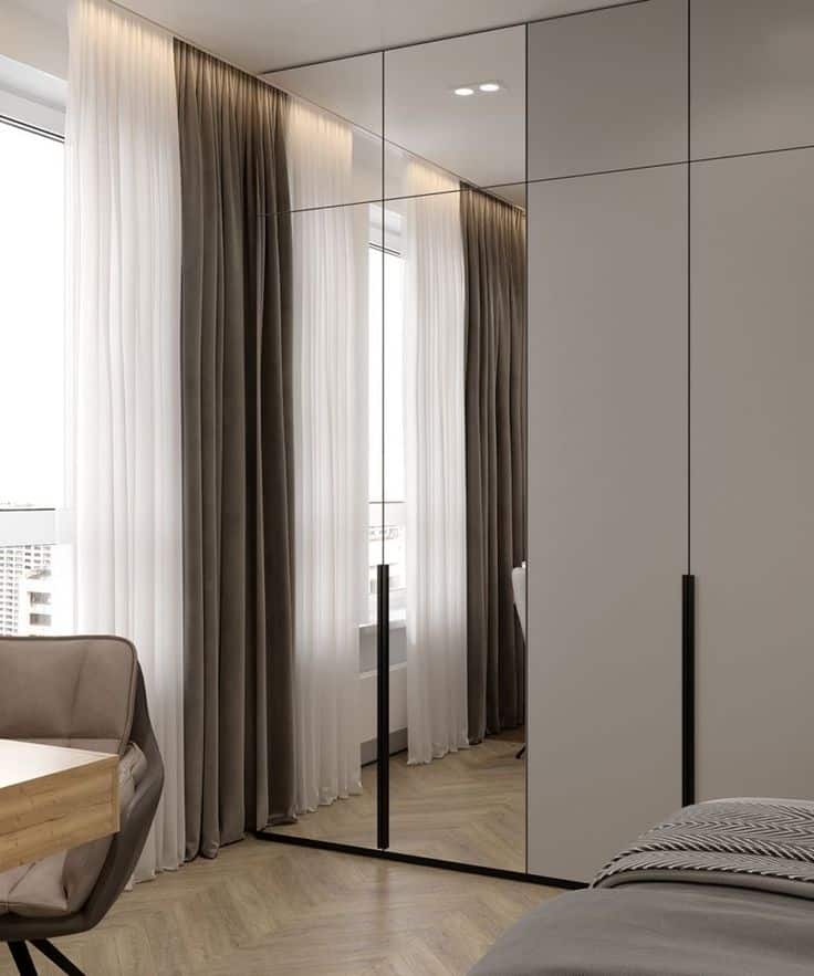 ba8fb13a-4716-452c-b8e5-7b570b04a704 Modern bedroom with large mirrored wardrobe, soft lighting, gray curtains, and wooden flooring, creating a sleek design. | Sky Rye Design Modern bedroom with large mirrored wardrobe, soft lighting, gray curtains, and wooden flooring, creating a sleek design.