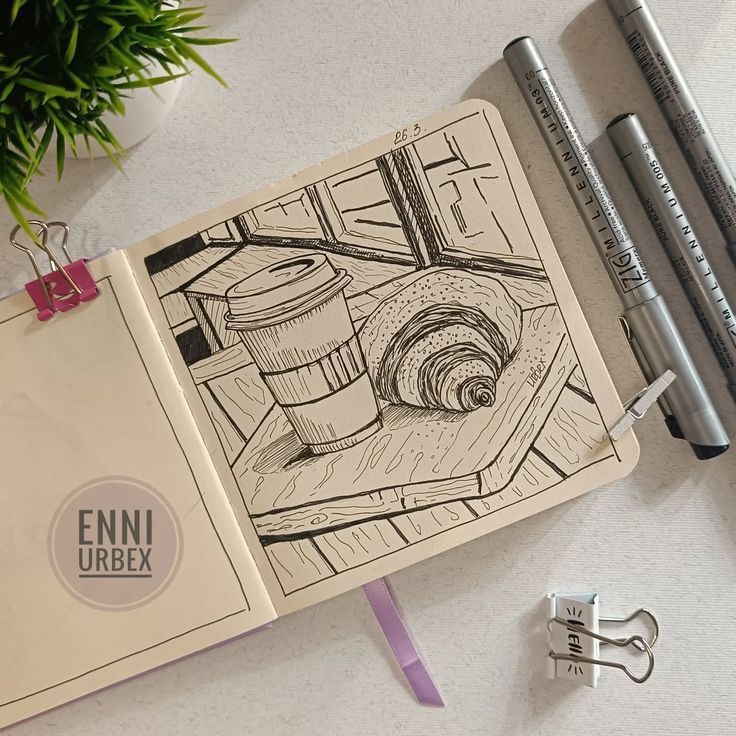 bb5c6013-02ac-43c3-806f-7ce90de974b7 Sketch of coffee and croissant in notebook, surrounded by pens on a table. | Sky Rye Design Sketch of coffee and croissant in notebook, surrounded by pens on a table.