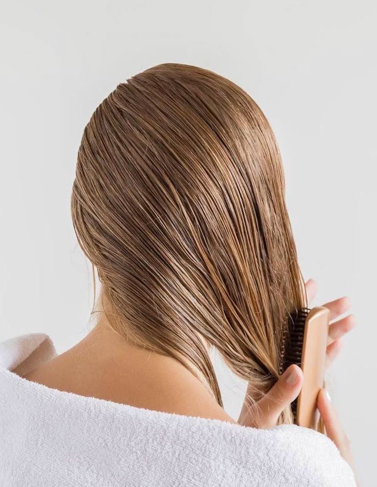 Person combing smooth, wet hair with a wooden brush, wrapped in a white towel, showcasing hair care routine.