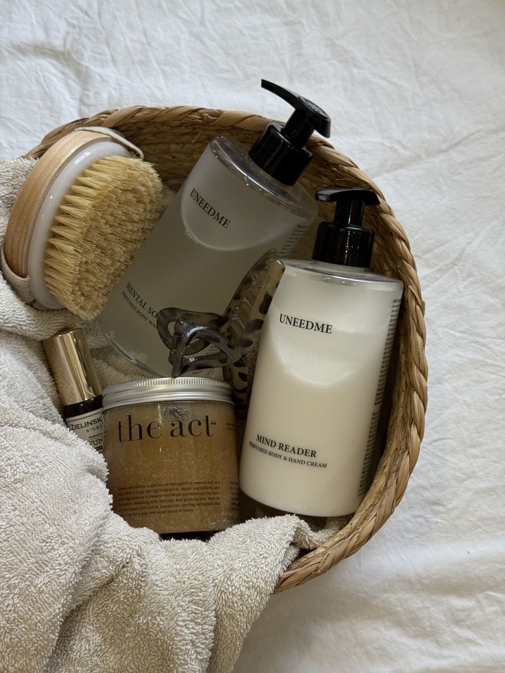 Basket with skincare essentials: lotion, body scrub, brush, towel, and a hair clip on a white background.