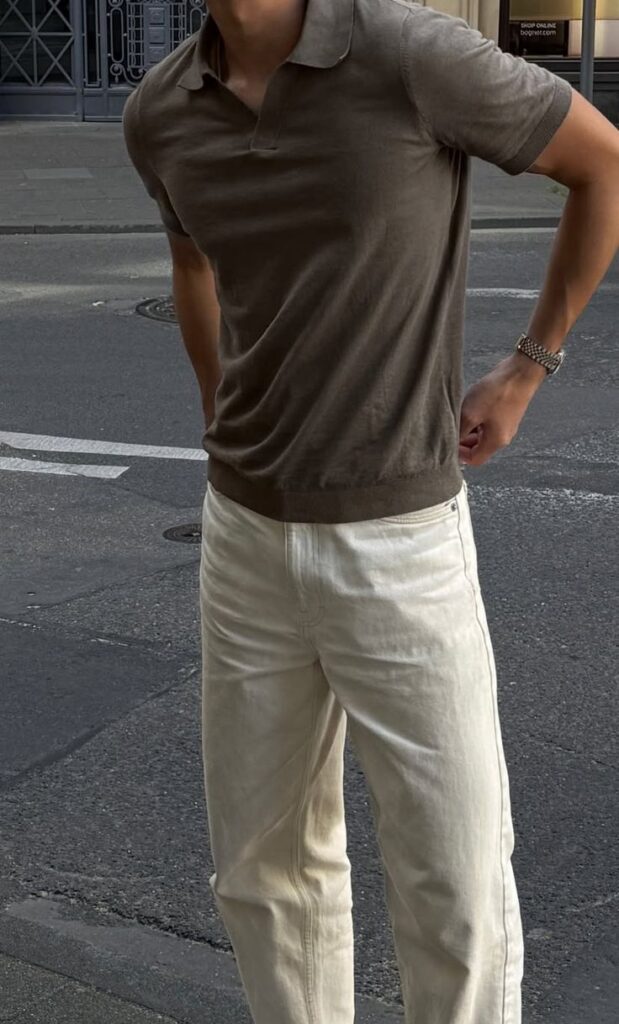 Man in a brown shirt and cream pants stands on a city street, wearing a silver watch, casual fashion style.