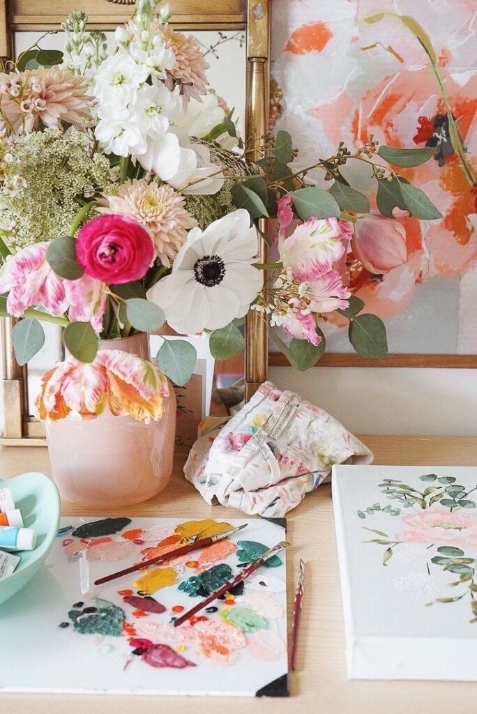Colorful floral arrangement with painting tools and canvas on a wooden table, showcasing artistic creativity and nature.