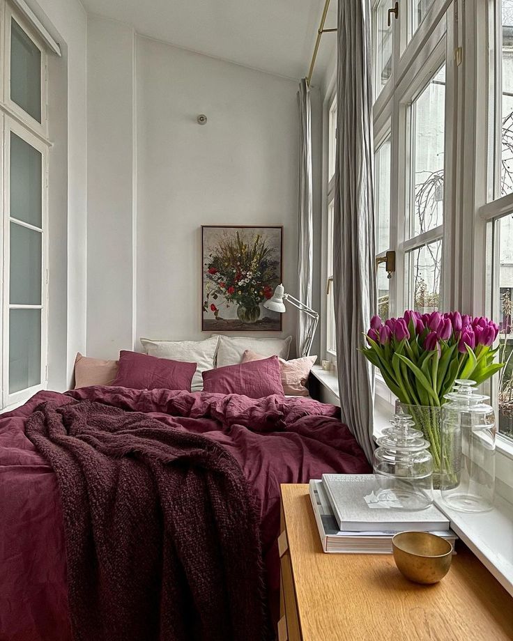 bedroom inspo Cozy bedroom with burgundy bedding, large windows, tulip vase, and a floral painting, creating a serene, inviting space. | Sky Rye Design Cozy bedroom with burgundy bedding, large windows, tulip vase, and a floral painting, creating a serene, inviting space.
