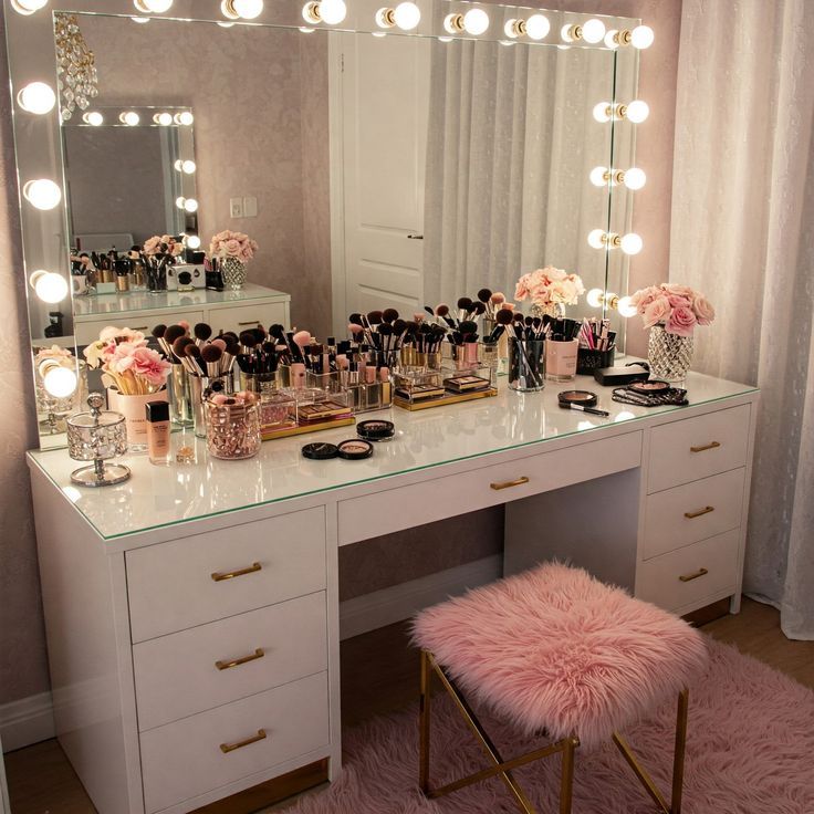 bffe6aae-4d56-4463-a196-2e6b94f878d8 Chic vanity table with illuminated mirror, makeup collection, pink flowers, and plush fur stool creating a stylish setup. | Sky Rye Design Chic vanity table with illuminated mirror, makeup collection, pink flowers, and plush fur stool creating a stylish setup.