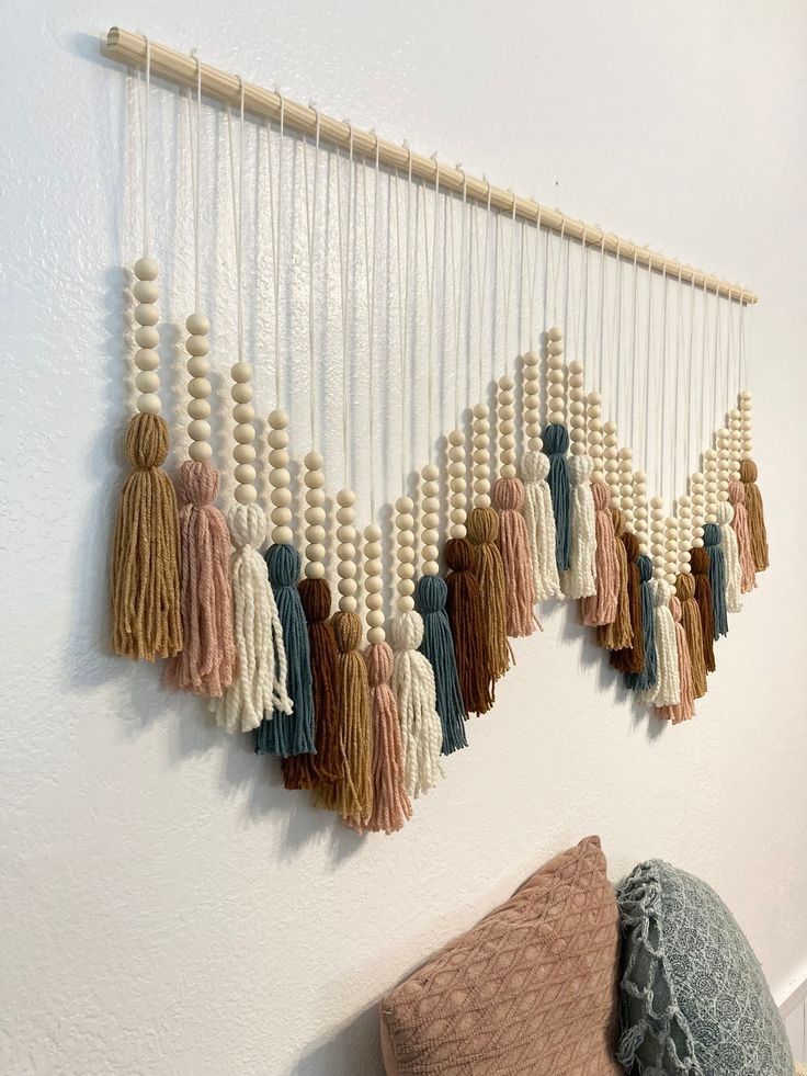 boho wall art Bohemian wall hanging with colorful yarn tassels and wooden beads in a chevron pattern above textured pillows. | Sky Rye Design Bohemian wall hanging with colorful yarn tassels and wooden beads in a chevron pattern above textured pillows.