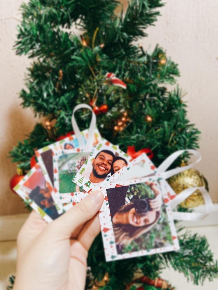 Hand holds photo garland in front of Christmas tree, showcasing festive holiday memories.