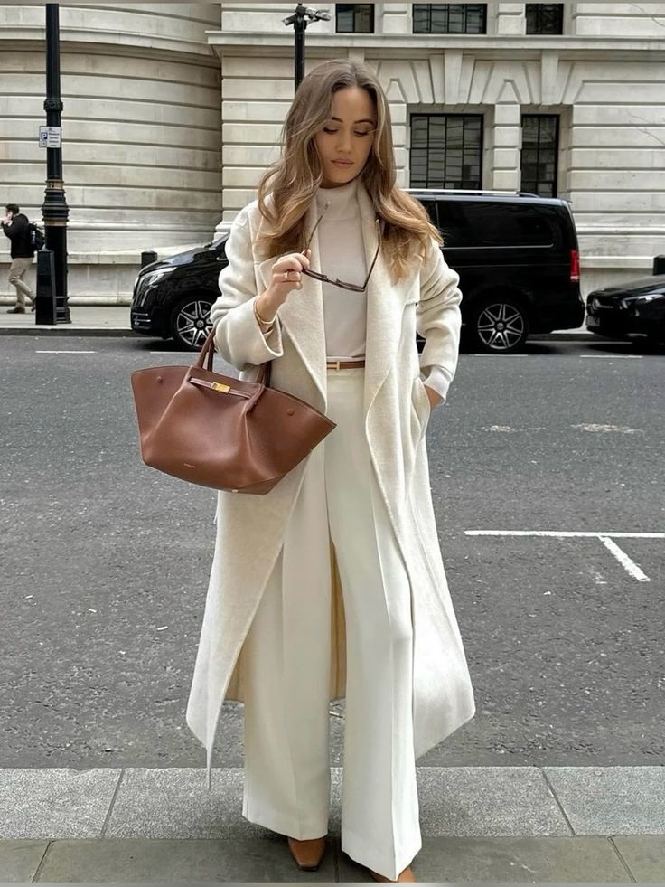 c5995c80-3bc5-4ade-a997-5455dc7e634f Woman in stylish white outfit and coat holding a brown handbag on a city street. | Sky Rye Design Woman in stylish white outfit and coat holding a brown handbag on a city street.