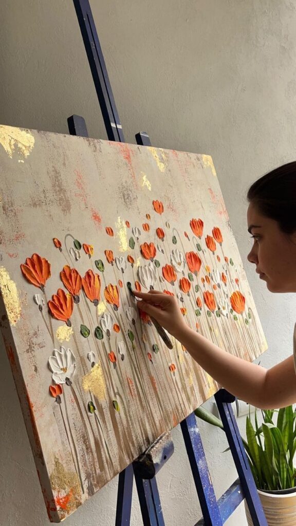 c769a664-69ea-46f7-96bd-b7734f94dfad Artist painting textured floral artwork on canvas, with vibrant orange and white flowers. | Sky Rye Design Artist painting textured floral artwork on canvas, with vibrant orange and white flowers.