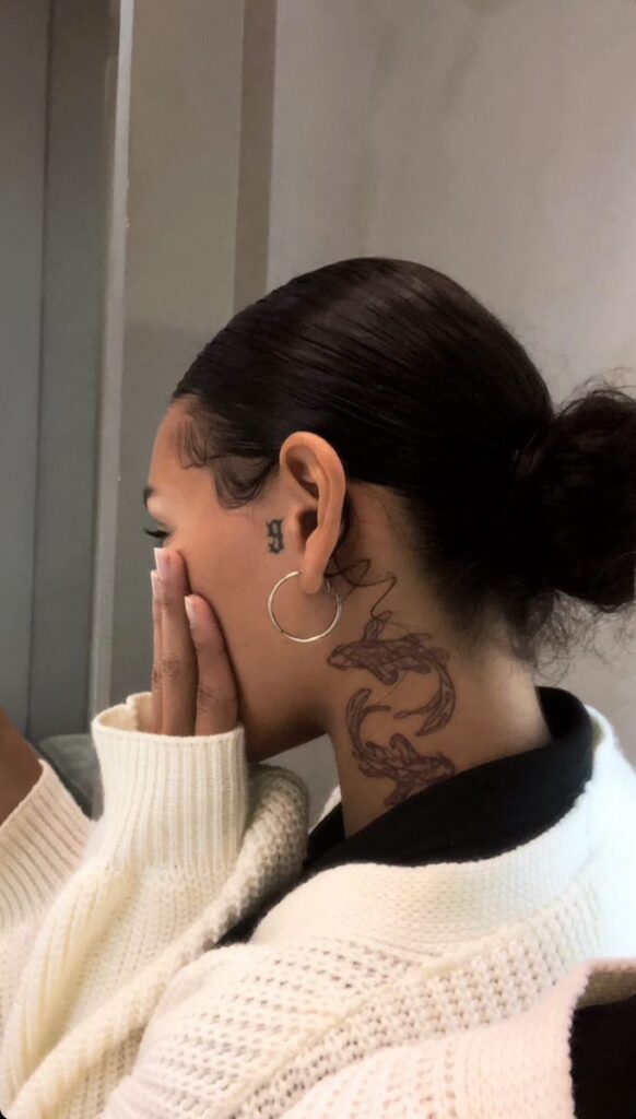 c7fd8bcd810998fcfe8ccad6b1a8a624 Woman with bun and hoop earrings shows neck tattoos, wearing cream sweater. | Sky Rye Design Woman with bun and hoop earrings shows neck tattoos, wearing cream sweater.