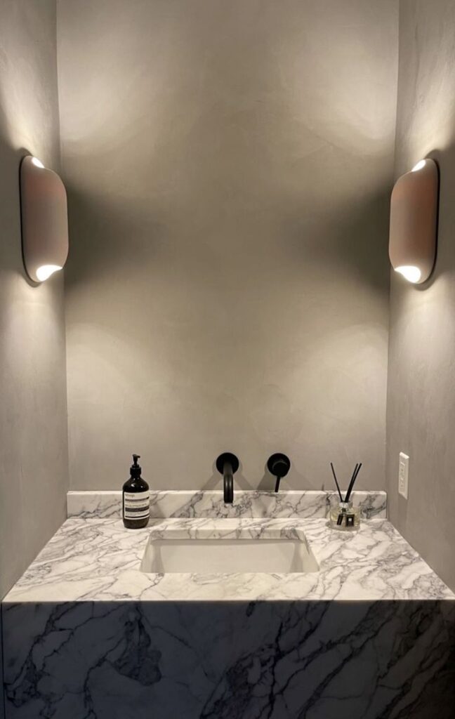 Modern marble sink with sleek black faucet, dim wall lighting, and stylish accessories in a minimalist bathroom design.