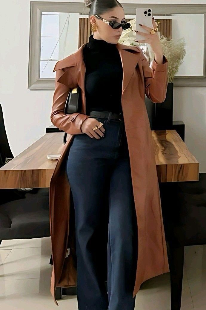 cdd2bbff-d45d-4dea-9fcb-006ccfb83260 Woman in stylish trench coat and sunglasses taking a mirror selfie in modern room. | Sky Rye Design Woman in stylish trench coat and sunglasses taking a mirror selfie in modern room.