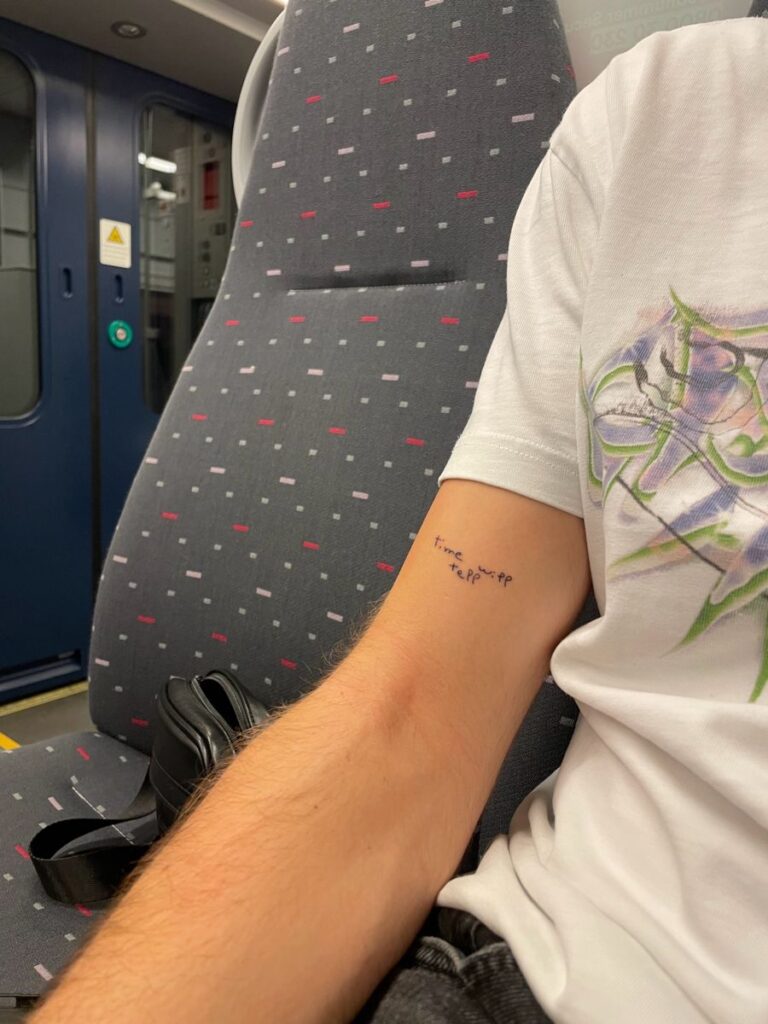 ceb22dae6621f613fa25180caa9ca712 Person on a train seat with a small text tattoo on arm, next to a black bag. Casual travel scene. | Sky Rye Design Person on a train seat with a small text tattoo on arm, next to a black bag. Casual travel scene.