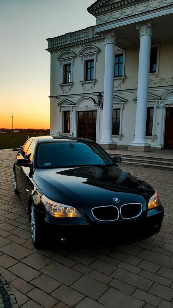 Black BMW parked in front of a classic mansion at sunset, showcasing elegance and luxury.