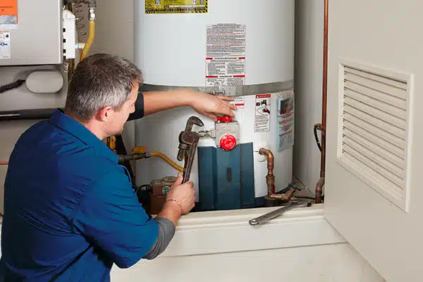 Technician repairing a hot water heater, adjusting settings with tools in a utility room.