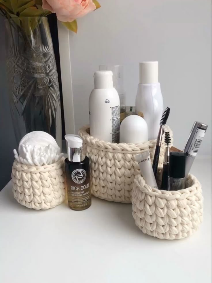 crochet Woven baskets holding skincare and makeup products on a white surface, next to a decorative vase with flowers. | Sky Rye Design Woven baskets holding skincare and makeup products on a white surface, next to a decorative vase with flowers.