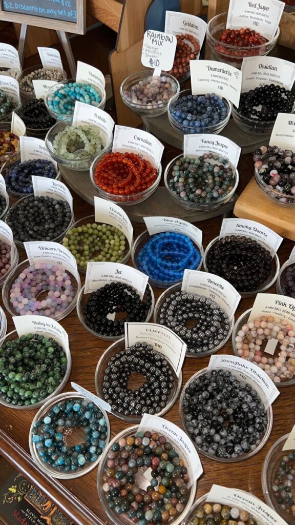 Colorful gemstone bracelets on display in bowls with price tags and labels in a store setting.