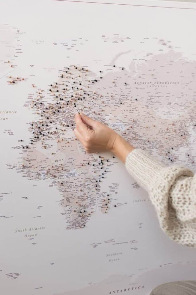 Hand placing pins on a world map, marking travel destinations, wearing a knitted sweater.