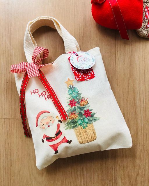 Festive Christmas tote bag with Santa, tree design, red bows, tag, on wooden floor. Perfect holiday gift wrapping.