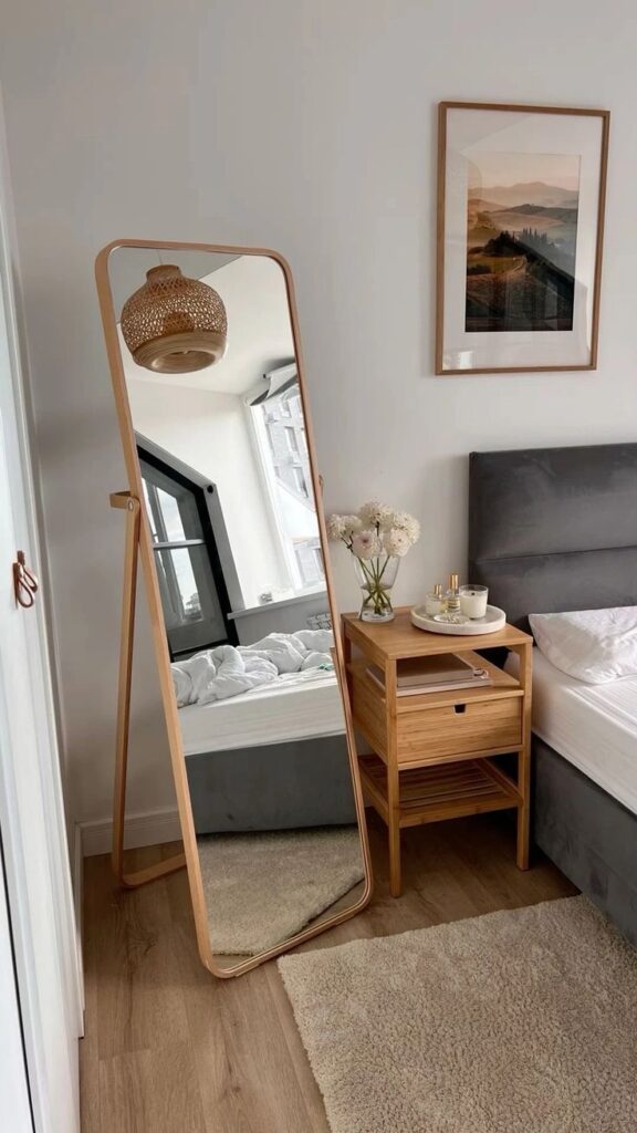 Modern bedroom with wooden mirror, cozy decor, and bedside table with flowers. Minimalist style and natural lighting.