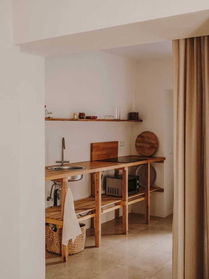 Minimalist wooden kitchen with open shelves, a sink, microwave, and a curtain, creating a cozy, rustic atmosphere.