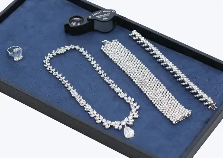 diamond-jewelry-set Elegant diamond jewelry set with necklace, bracelets, and ring on display with a magnifying glass. | Sky Rye Design Elegant diamond jewelry set with necklace, bracelets, and ring on display with a magnifying glass.