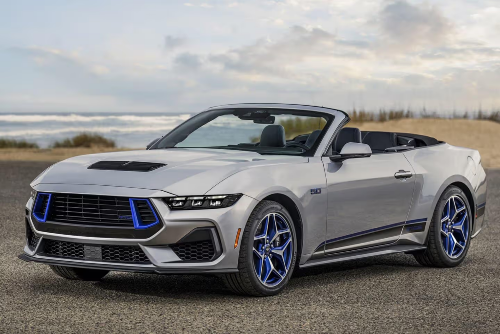 image Silver convertible sports car with blue-accent wheels parked on coastal road with ocean and dunes backdrop | Sky Rye Design Silver convertible sports car with blue-accent wheels parked on coastal road with ocean and dunes backdrop