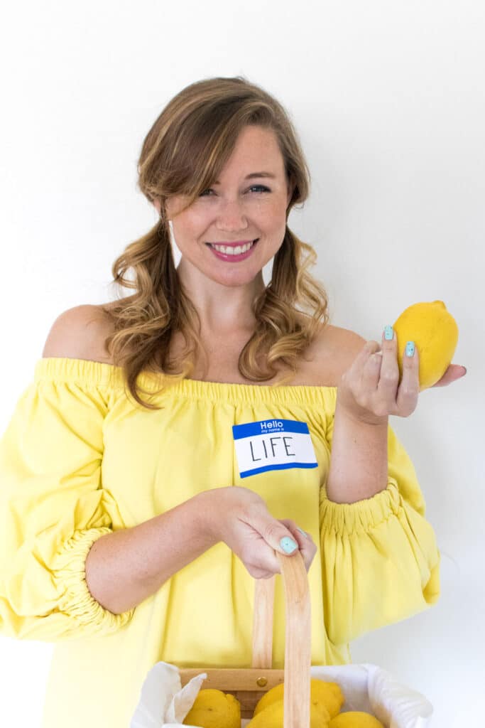 Woman in a yellow dress, holding a lemon basket, smiles with a Hello, my name is Life nametag.