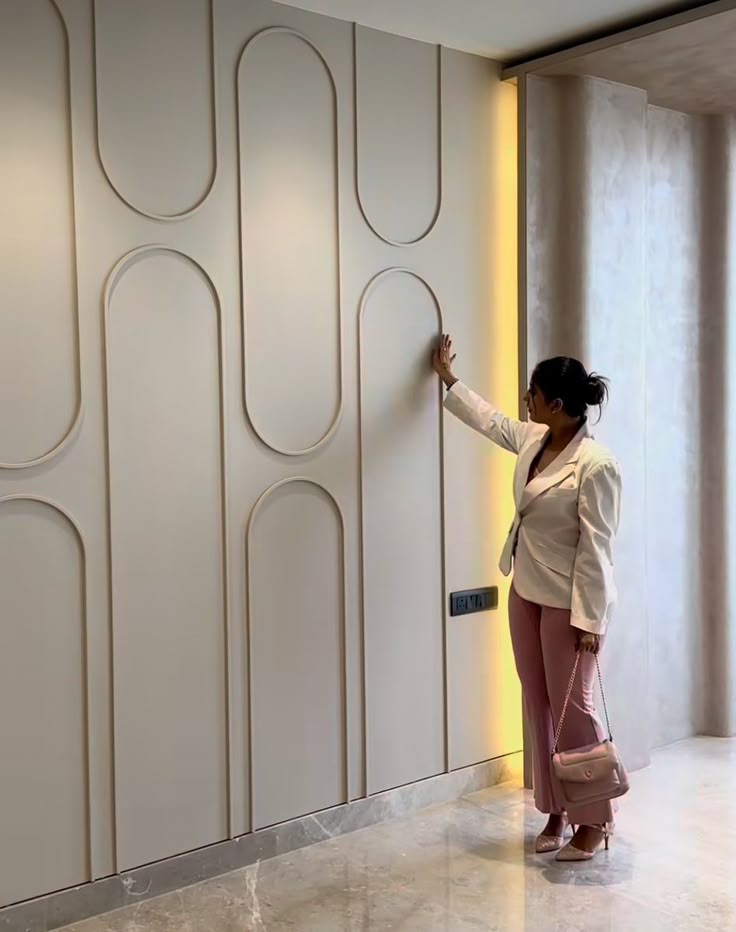e338a2a3-1cc5-4ab3-beae-38df37d42d23 Woman in stylish outfit touches modern wall design in elegant interior. | Sky Rye Design Woman in stylish outfit touches modern wall design in elegant interior.