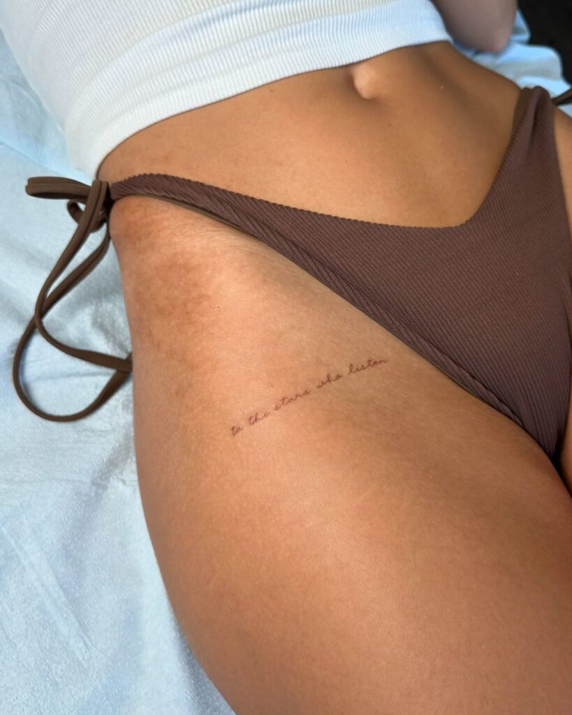e35461d1e1c47fe1af5534265ebfe904 Close-up of a woman in brown swimwear, showcasing a small cursive hip tattoo with the phrase to the stars who listen. | Sky Rye Design Close-up of a woman in brown swimwear, showcasing a small cursive hip tattoo with the phrase to the stars who listen.