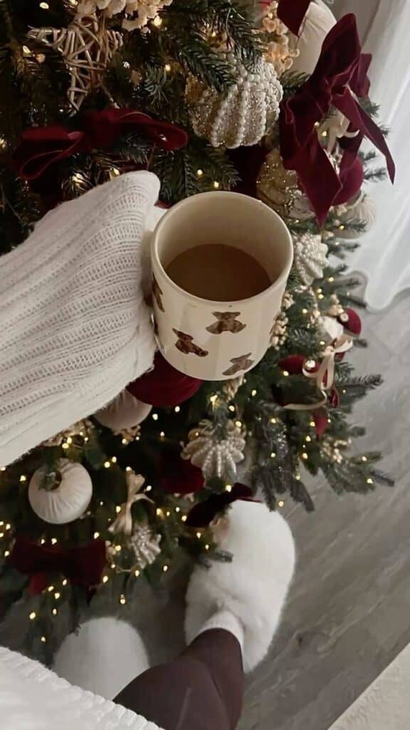 e64a9ba9-3fed-40ae-a730-c2e6eaa87829 Cozy winter morning with a warm drink by a decorated Christmas tree in white and burgundy ornaments and fluffy slippers. | Sky Rye Design Cozy winter morning with a warm drink by a decorated Christmas tree in white and burgundy ornaments and fluffy slippers.